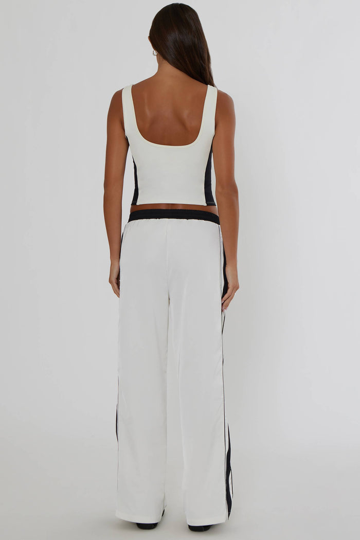 A woman shown from the back wearing a white sleeveless crop top and matching wide-leg pants with black side panels and a black waistband, against a plain light gray studio background.