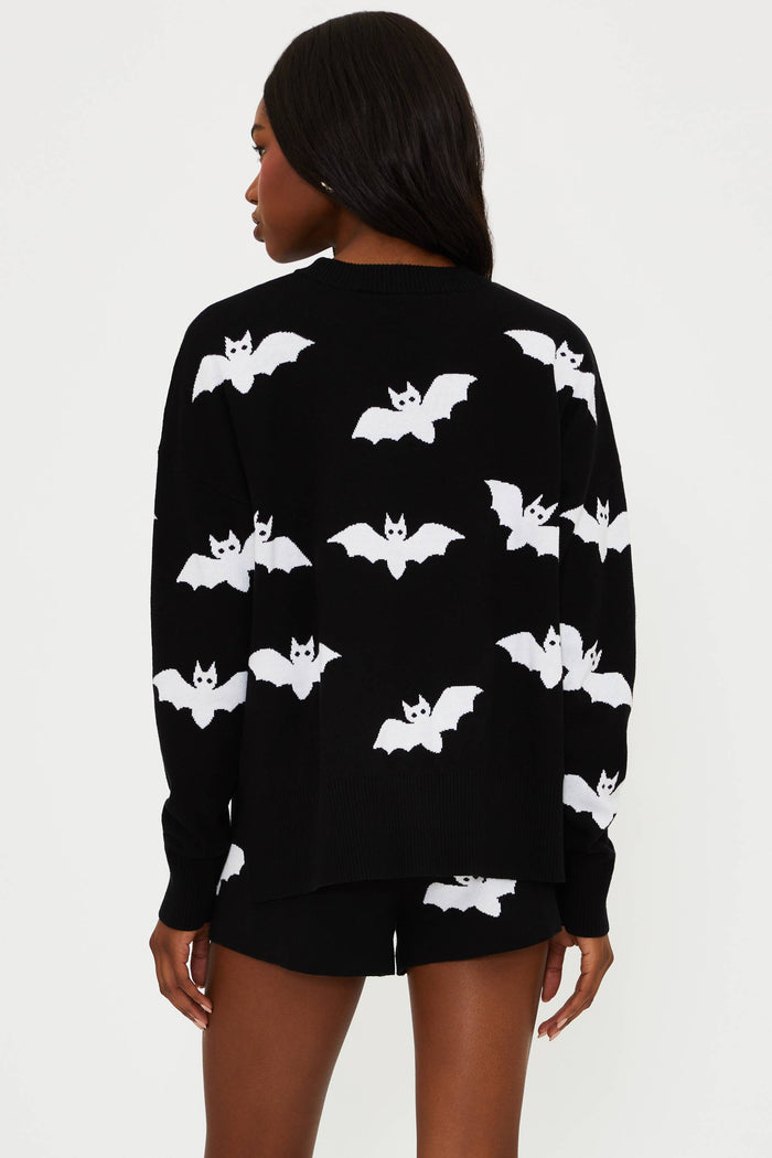 Person wearing a black sweater with white bat patterns on a plain background