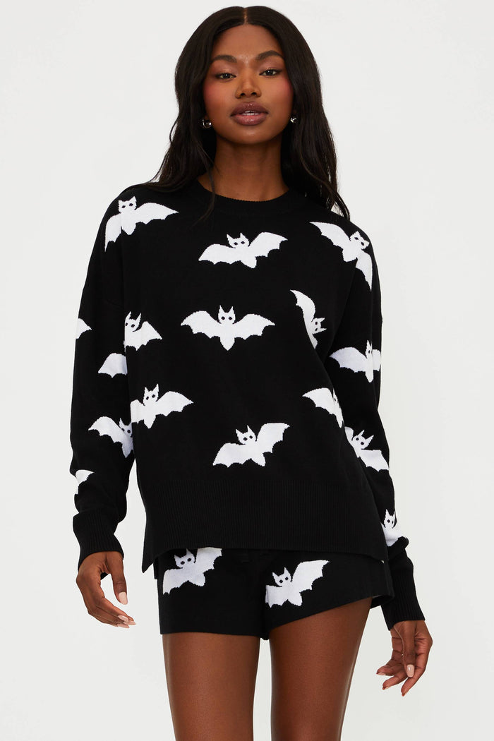 Woman wearing a black sweater with white bat patterns and black shorts on a white background