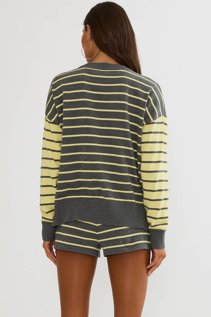 A woman shown from the back wearing a dark gray and light yellow striped long-sleeve top and matching shorts against a plain light gray studio background.