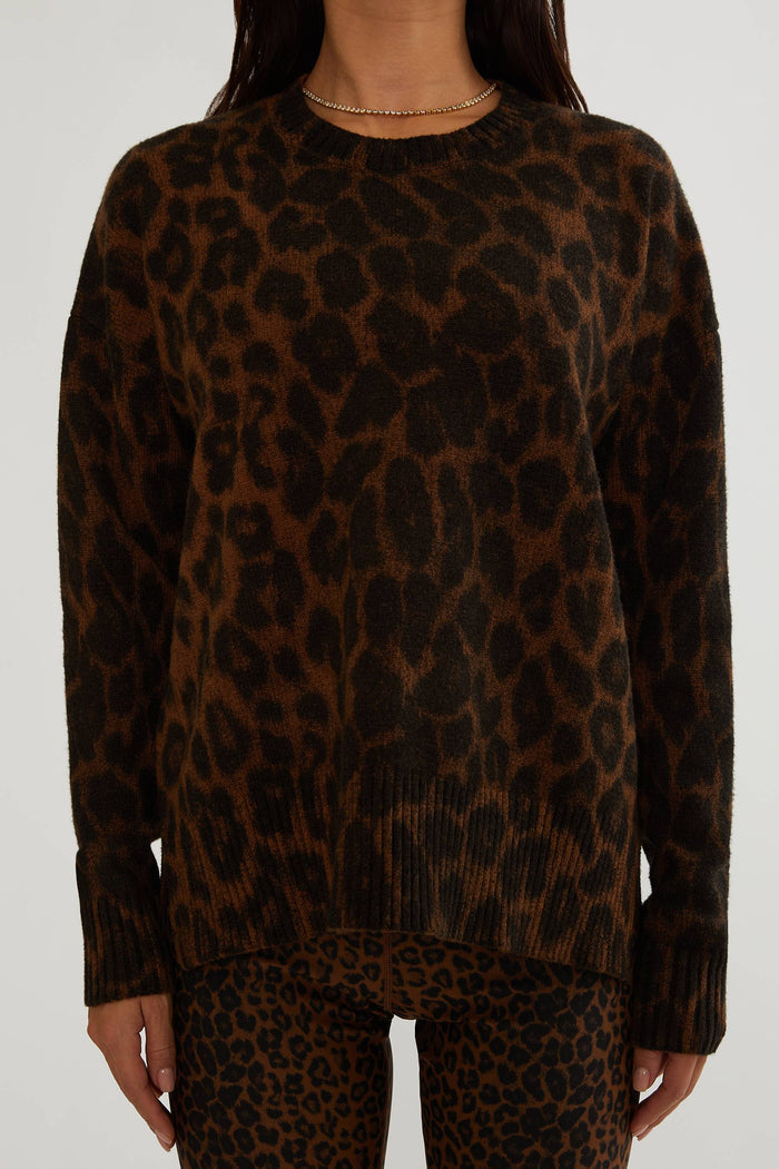A woman wearing a brown and black leopard-print knit sweater and matching leopard-print pants against a plain light gray background.