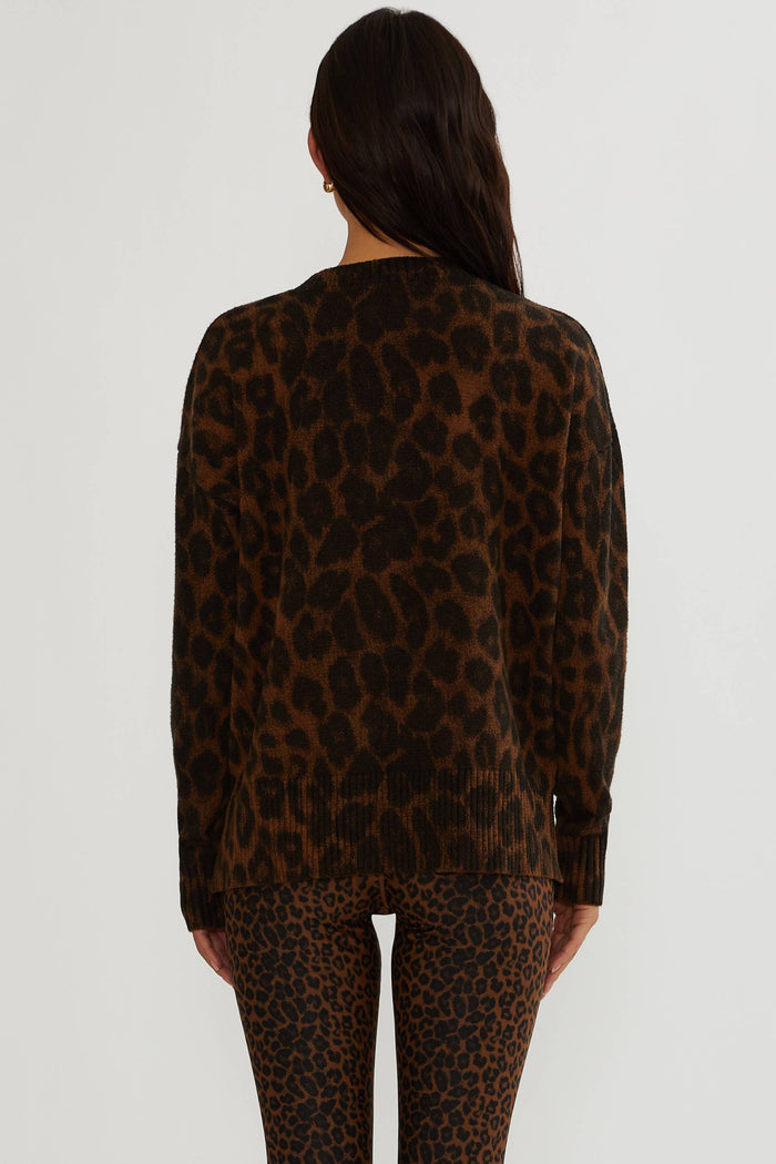 A woman shown from the back wearing a brown and black leopard print knit sweater and matching leopard print leggings against a plain light gray studio background.