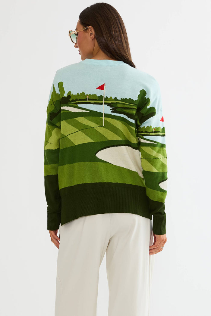 Woman wearing a sweater with a golf course design on a plain background