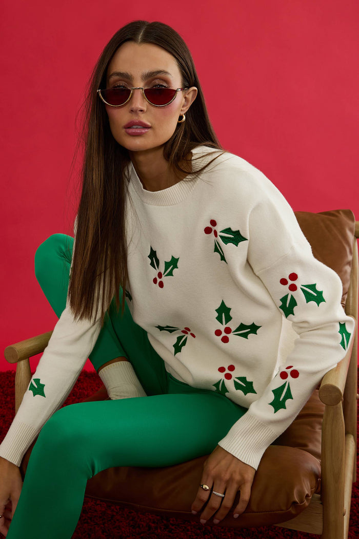 Woman wearing a white sweater with holly pattern.