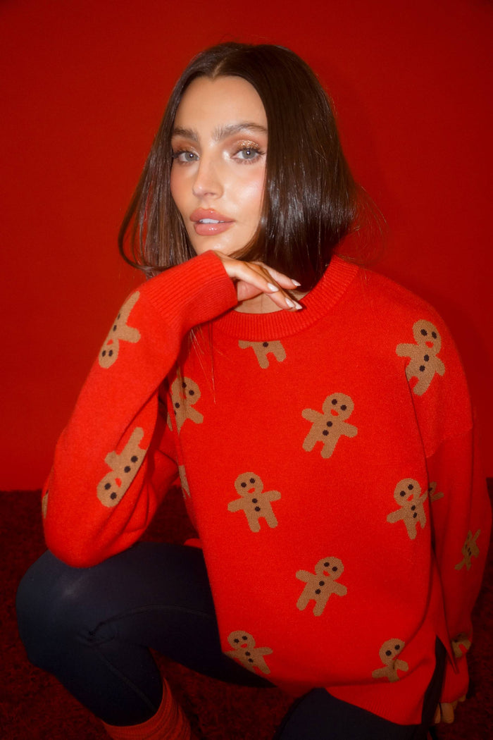 Person wearing a red sweater with gingerbread man patterns against a red background
