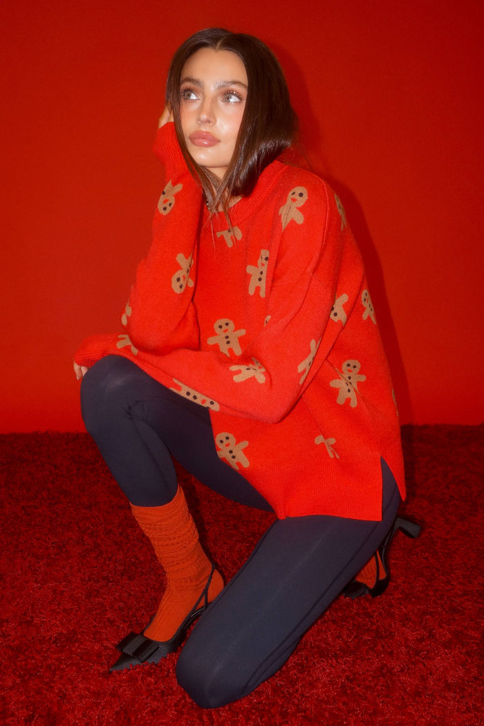 Woman wearing a red sweater with gingerbread man patterns on a white background