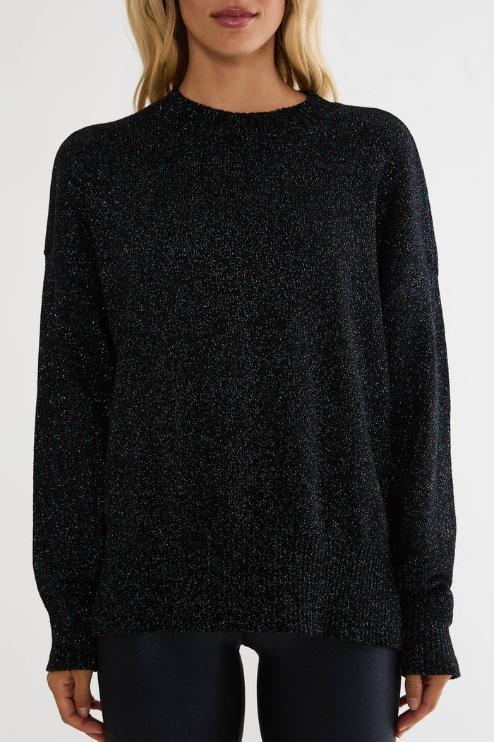 A woman wearing a black long-sleeve knit sweater with subtle glittery flecks, shown from the neck down against a plain light background.
