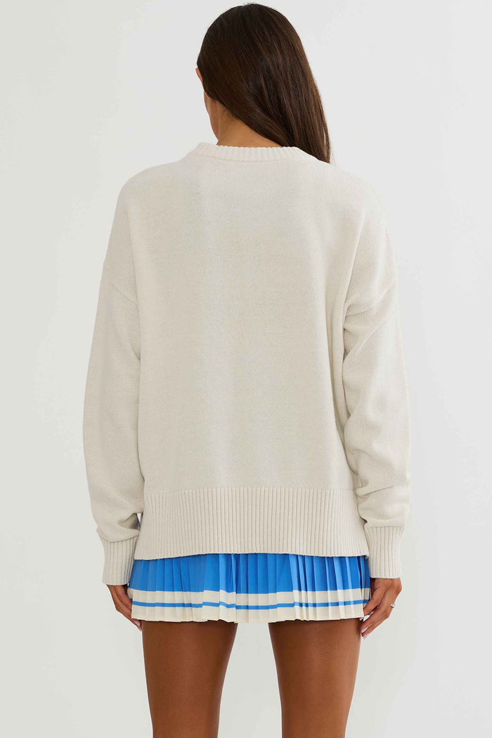 Woman wearing cream sweater with golf clubs on it.