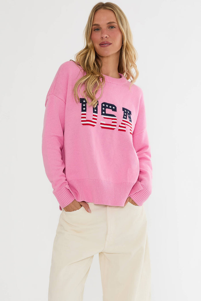 Woman wearing a pink sweater with 'USA' print on a white background