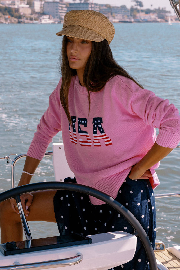 Woman on a boat wearing a pink sweater with 'USA' print and a straw hat.