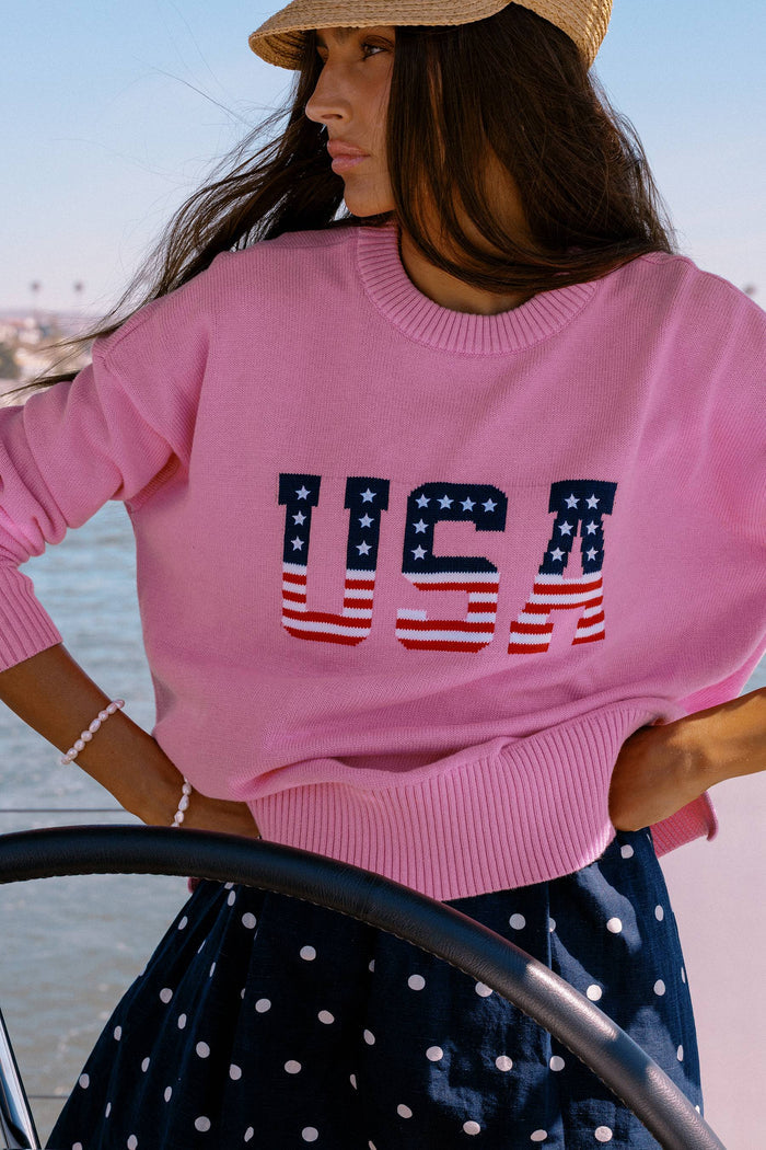 Woman wearing a pink sweater with 'USA' print by the water