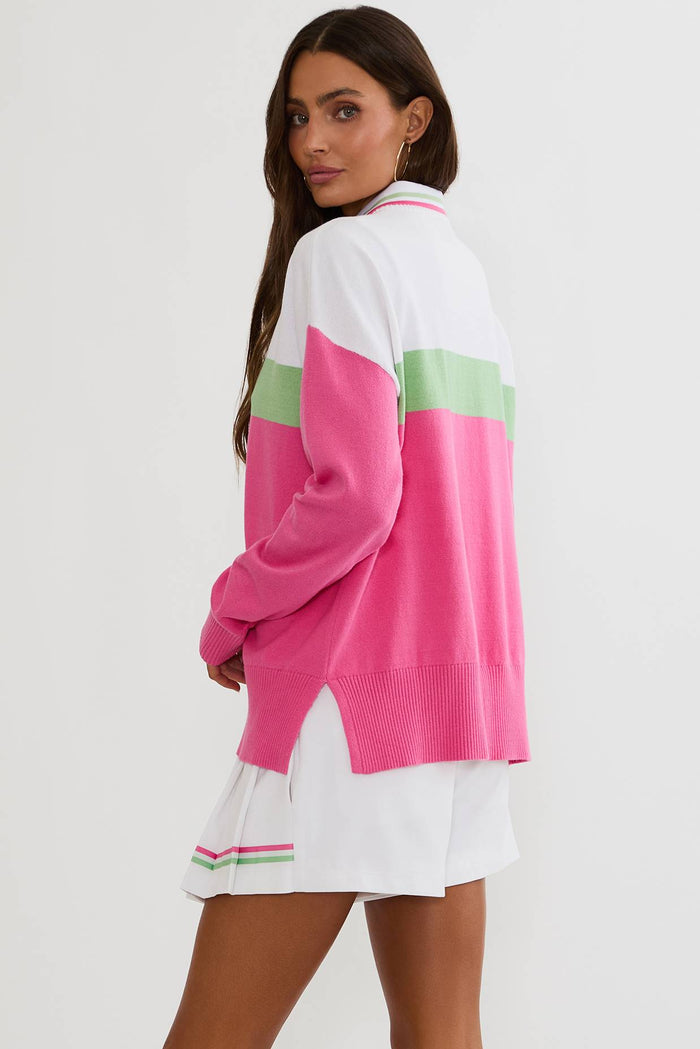 Woman wearing a pink and white sweater with green accents on a plain background