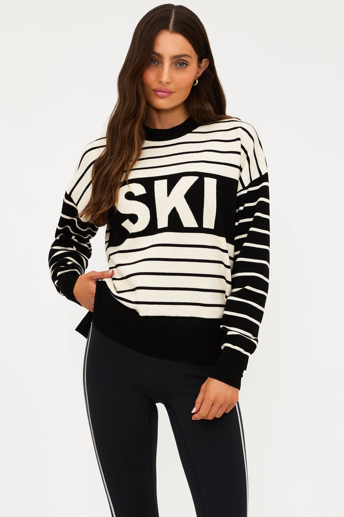 Woman wearing a black and white striped sweater with 'SKI' text on a plain background