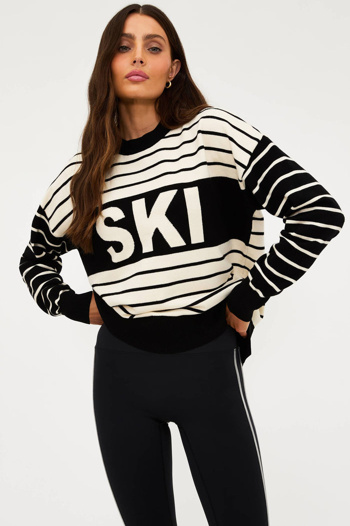 Woman wearing a black and white striped sweater with 'SKI' text on a plain background