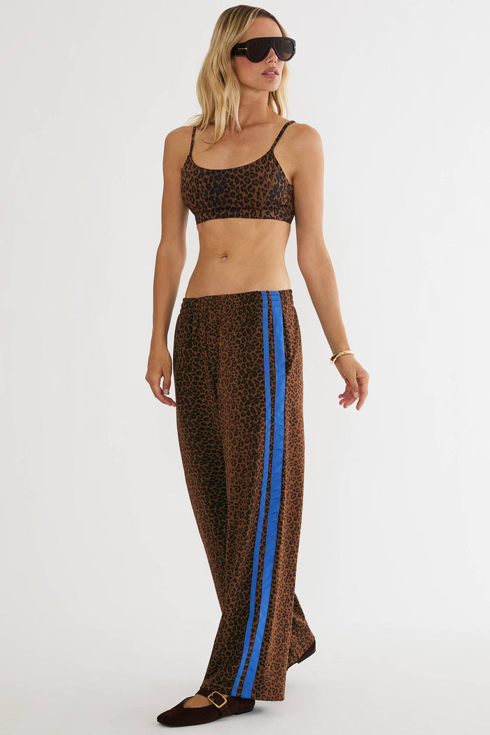 A woman modeling a matching two-piece leopard print set consisting of a cropped tank top and wide-leg pants with a bright blue side stripe, photographed against a plain white studio background.