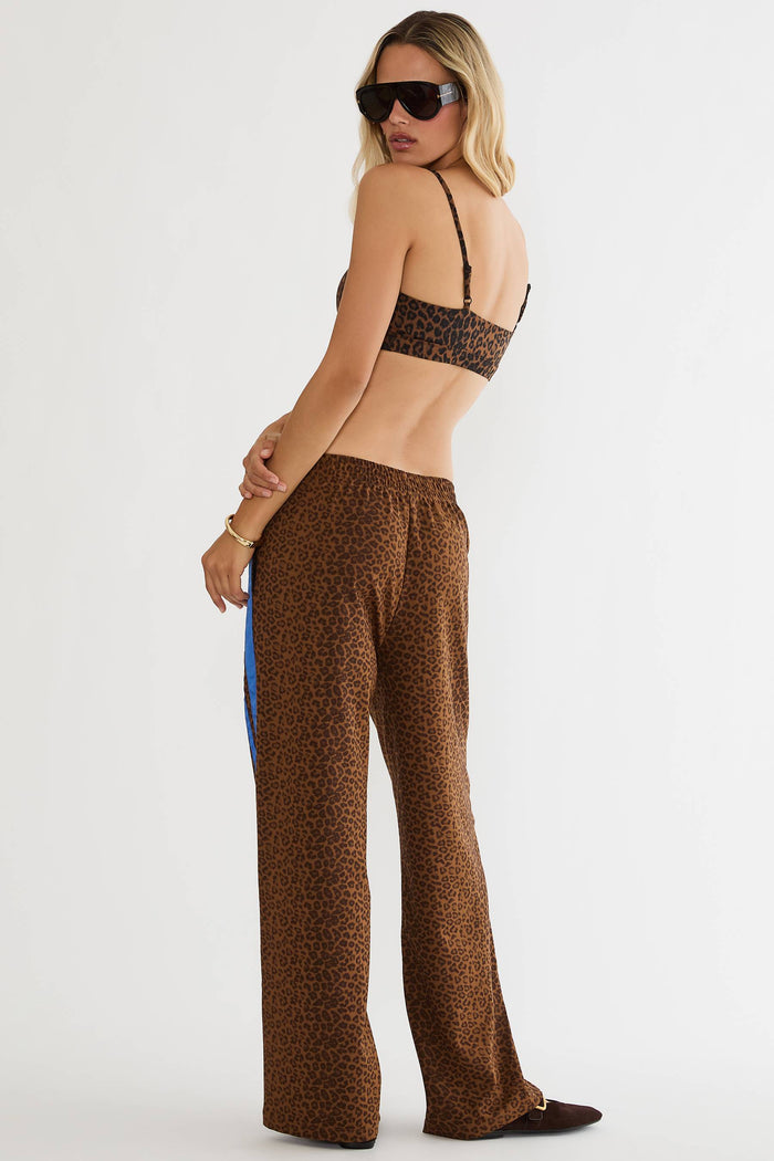 A woman modeling a matching brown leopard-print two-piece set consisting of a bikini top and wide-leg pants, photographed against a plain white studio background.