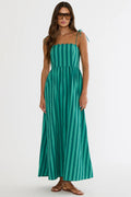 A woman modeling a green and teal vertically striped maxi dress with thin shoulder ties, styled with sunglasses and brown leather sandals against a plain white studio background.