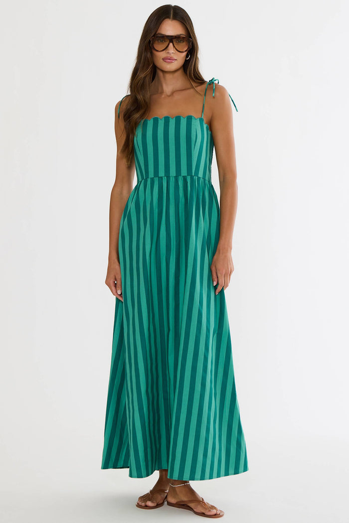 A woman modeling a green and teal vertically striped maxi dress with thin shoulder ties, styled with sunglasses and brown leather sandals against a plain white studio background.