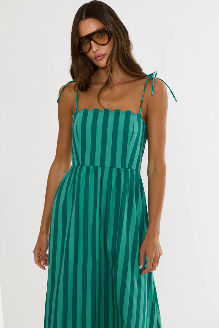 A woman modeling a green and teal vertically striped midi dress with thin shoulder ties, photographed against a plain light background.