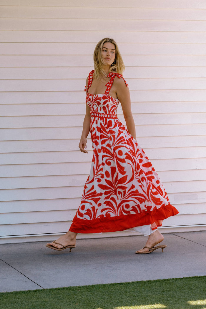 Woman wearing a red and white patterned dress against a white wall.