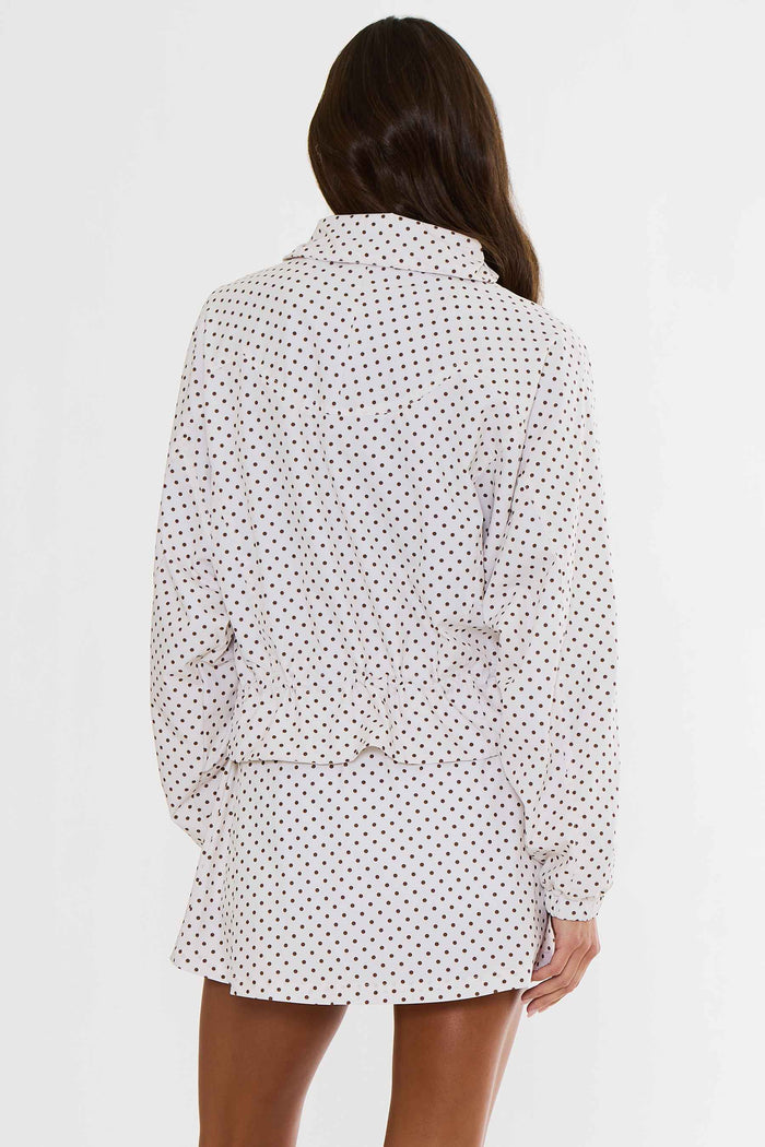 A woman shown from the back wearing a white long-sleeve collared shirt dress with a small black polka dot pattern, set against a plain white studio background.