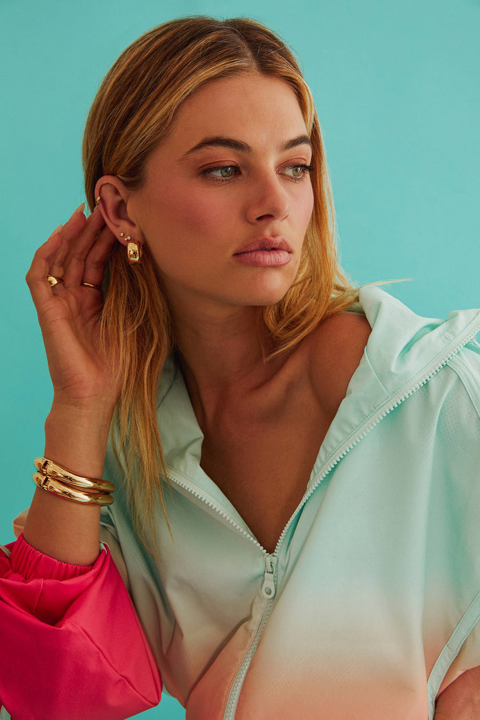 Woman wearing a light green jacket over a pink top against a teal background