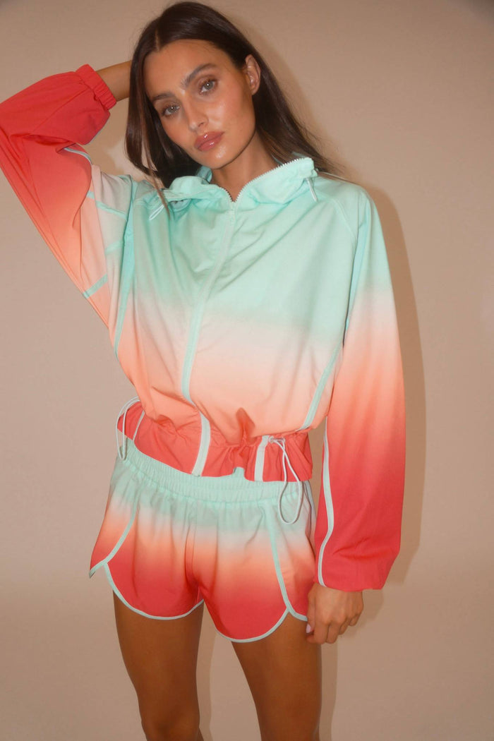 Person wearing a colorful ombre hoodie and shorts set against a beige background