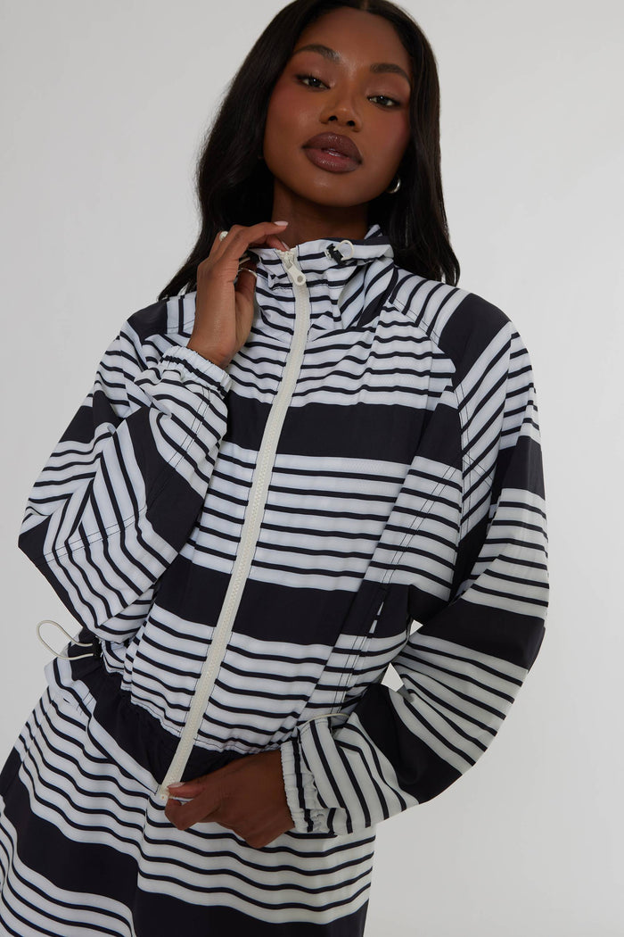 A woman wearing a black and white horizontally striped zip-up hoodie with a white drawstring, photographed against a plain light gray studio background.