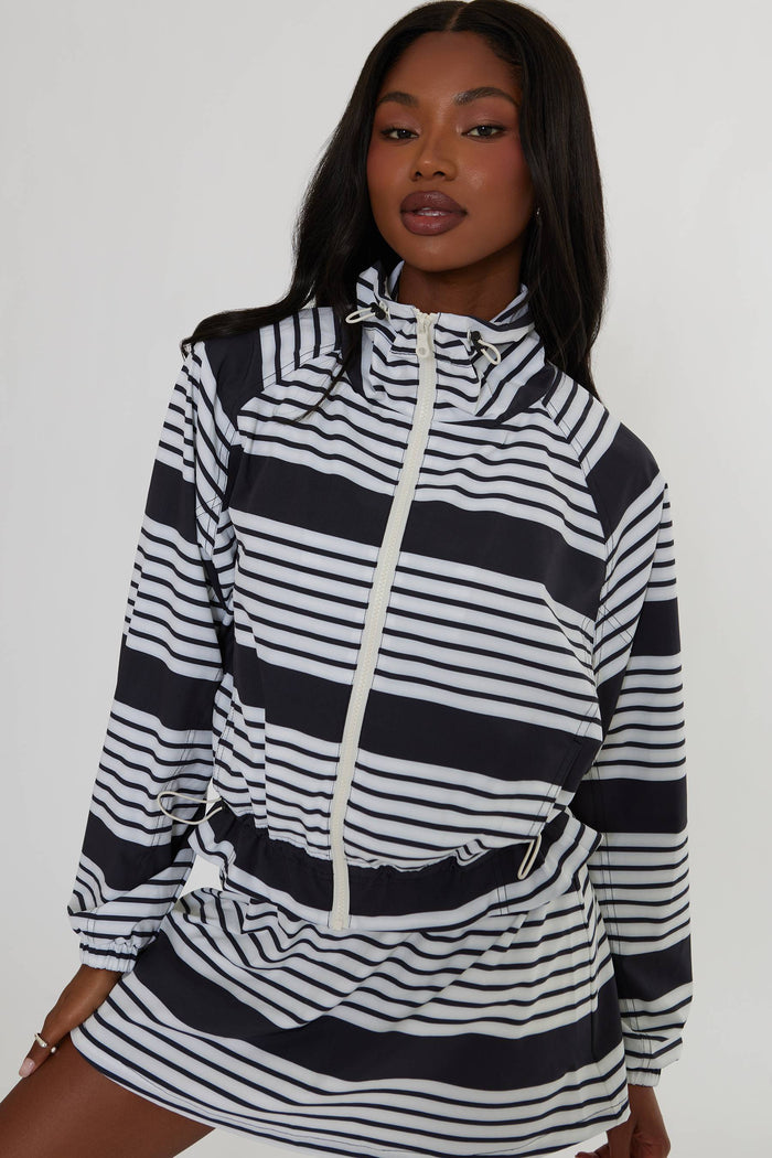 A woman wearing a black and white horizontally striped zip-up hoodie dress with a mock neck and drawstring waist, photographed against a plain light gray studio background.