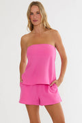 Woman wearing a pink strapless top and shorts set on a white background
