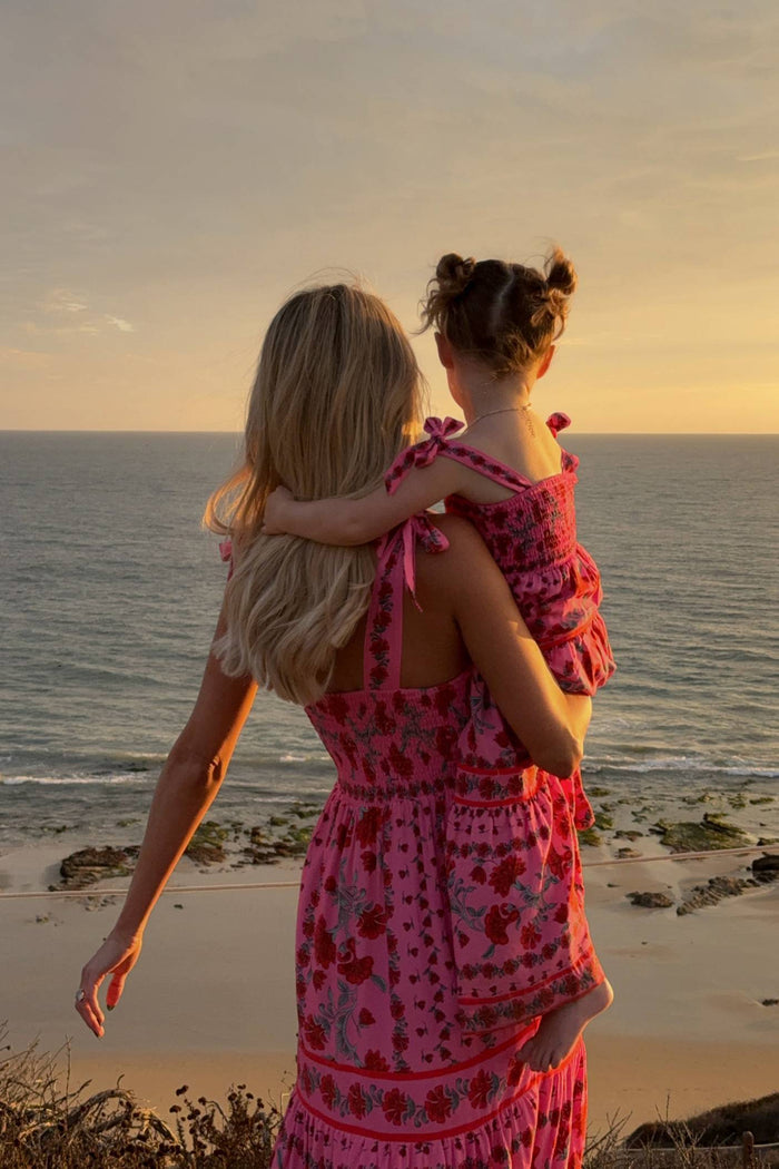Woman in a pink dress holding a child on a beach at sunset