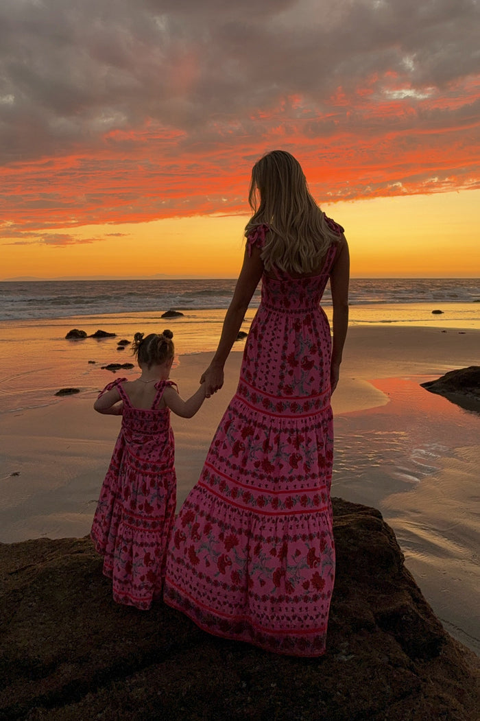 Woman and child in matching pink dresses standing on a beach at sunset.