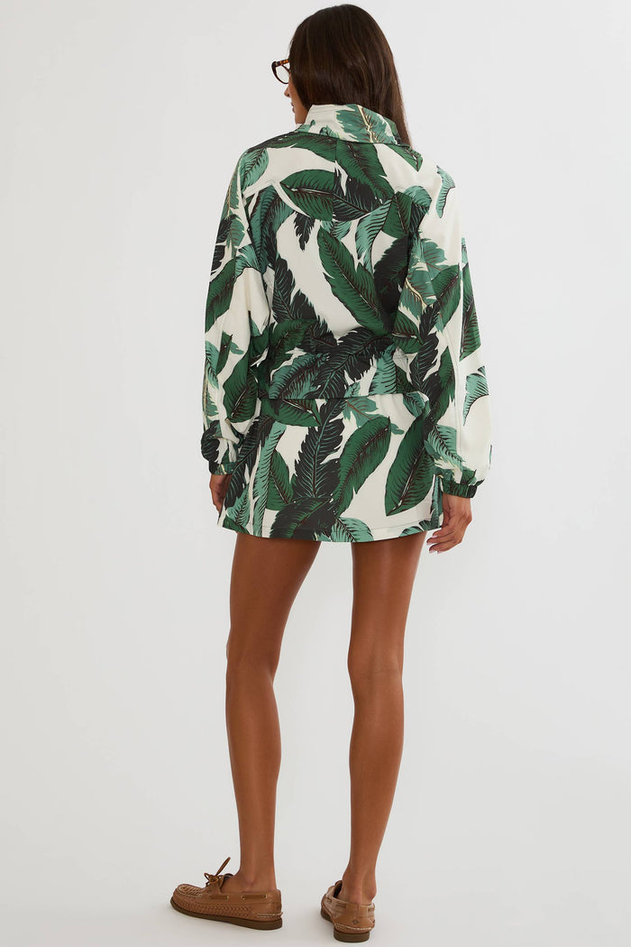 A woman shown from the back wearing a long-sleeve white shirt dress with a green tropical leaf print, paired with brown boat shoes, against a plain white studio background.