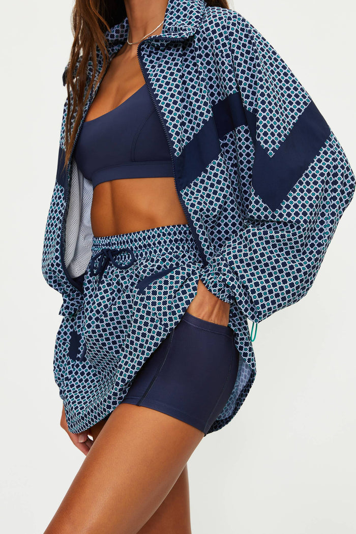 Person wearing a blue patterned cover-up over a sports bra and shorts on a white background