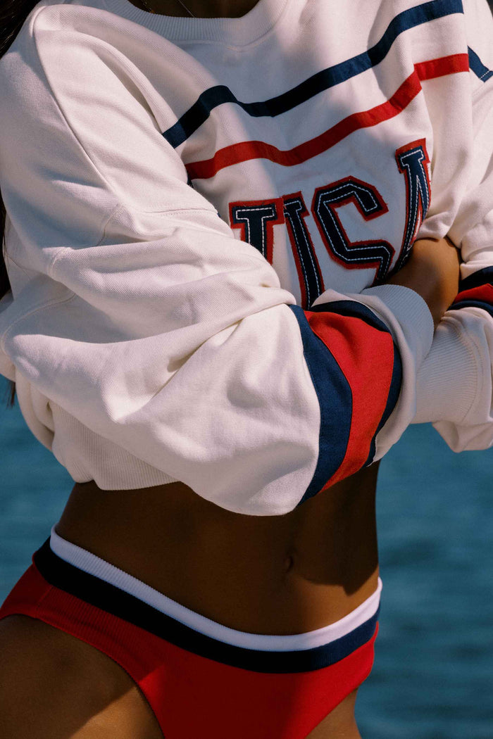 Person wearing a white sweatshirt with red and blue accents and red shorts against a blue background