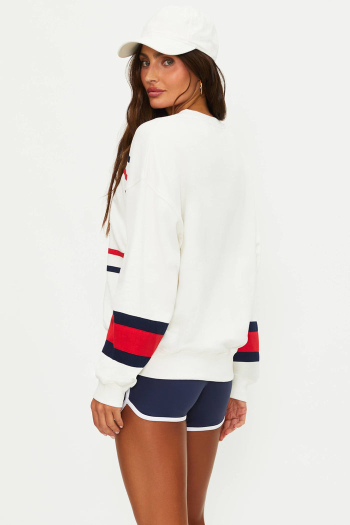 Woman wearing a white sweater with red and blue accents and navy shorts on a white background