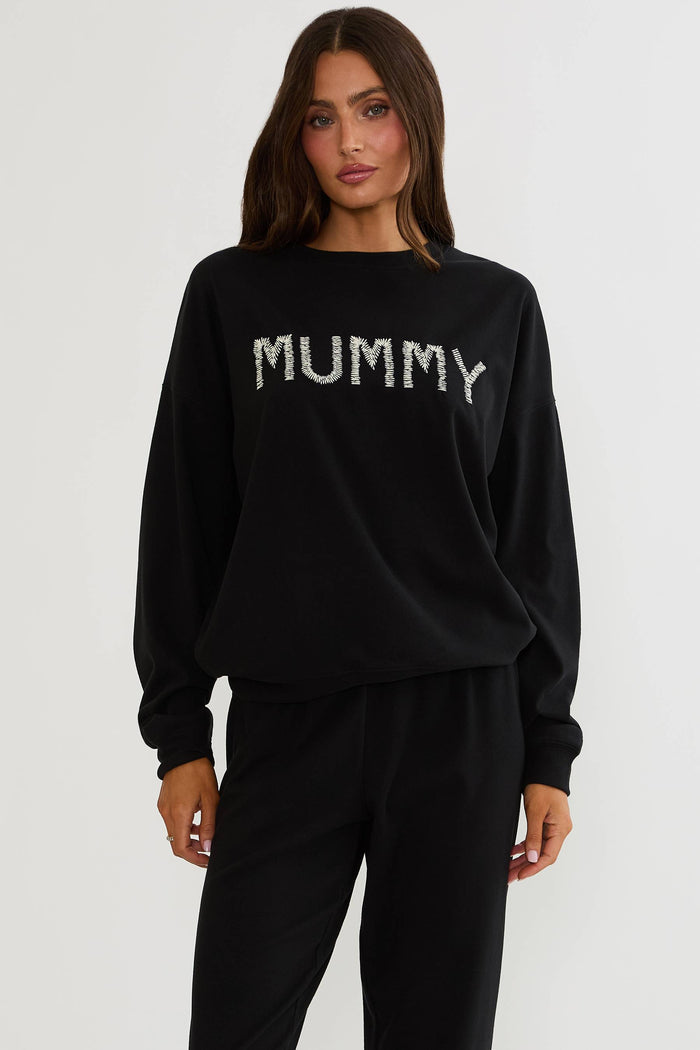 Black oversized sweatshirt with Halloween text "mummy" worn by a woman on a plain white background.