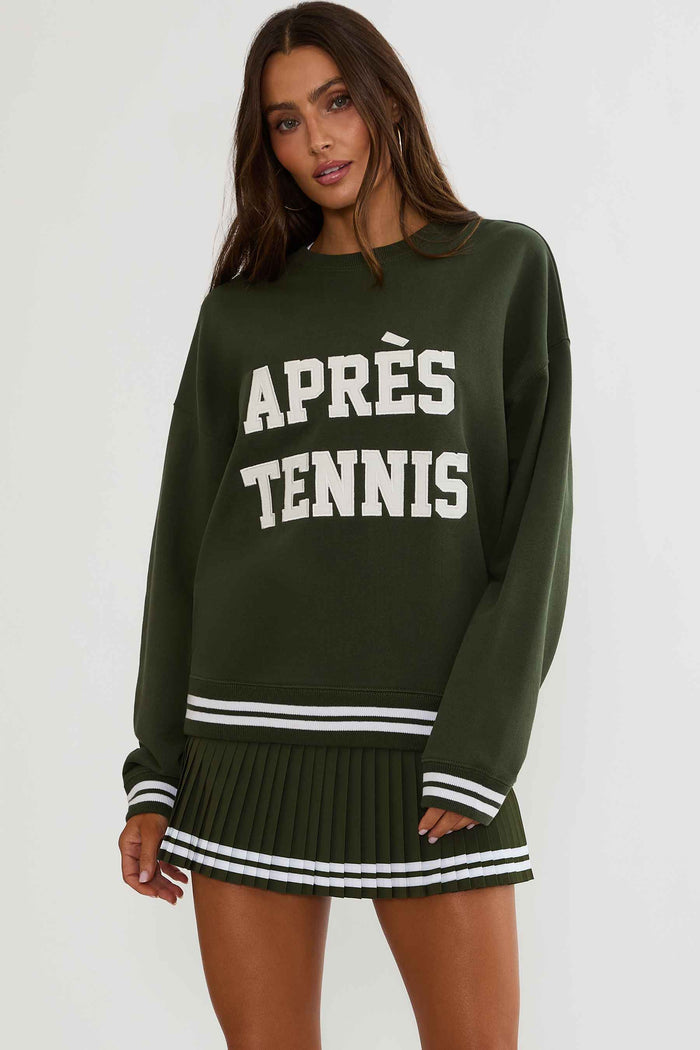 Woman wearing a green sweatshirt with white text "apres tennis"