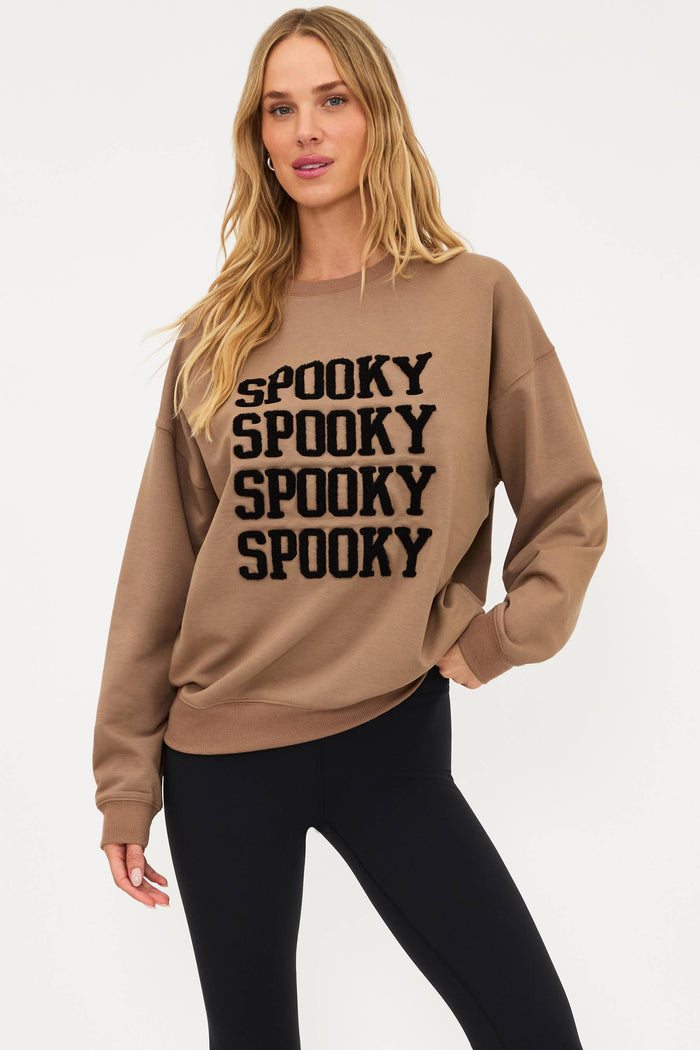 Woman wearing a beige sweatshirt with 'SPOOKY' text on a white background