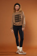 Woman wearing a beige sweatshirt with 'Spooky' text on a brown background