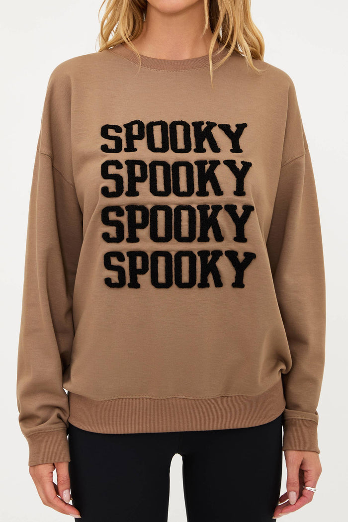 Woman wearing a beige sweatshirt with 'SPOOKY' text on a white background