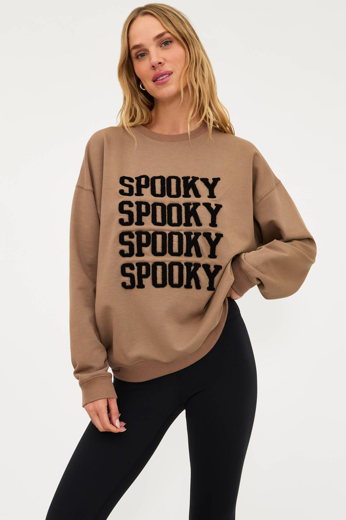 Woman wearing a beige sweatshirt with 'SPOOKY' text on a white background