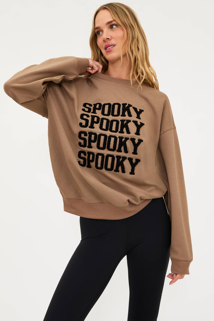 Woman wearing a beige sweatshirt with 'SPOOKY' text on a white background