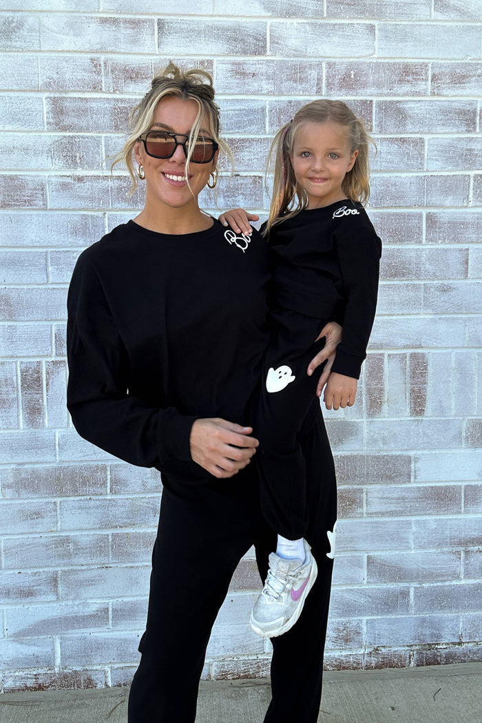 Woman holding a young girl both wearing black outfits against a brick wall.