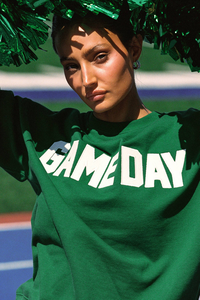 Person wearing a green 'GAME DAY' sweatshirt with green pom-poms in the background