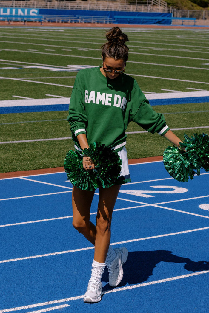Person in green 'GAME ON' sweatshirt with green pom-poms on a sports field