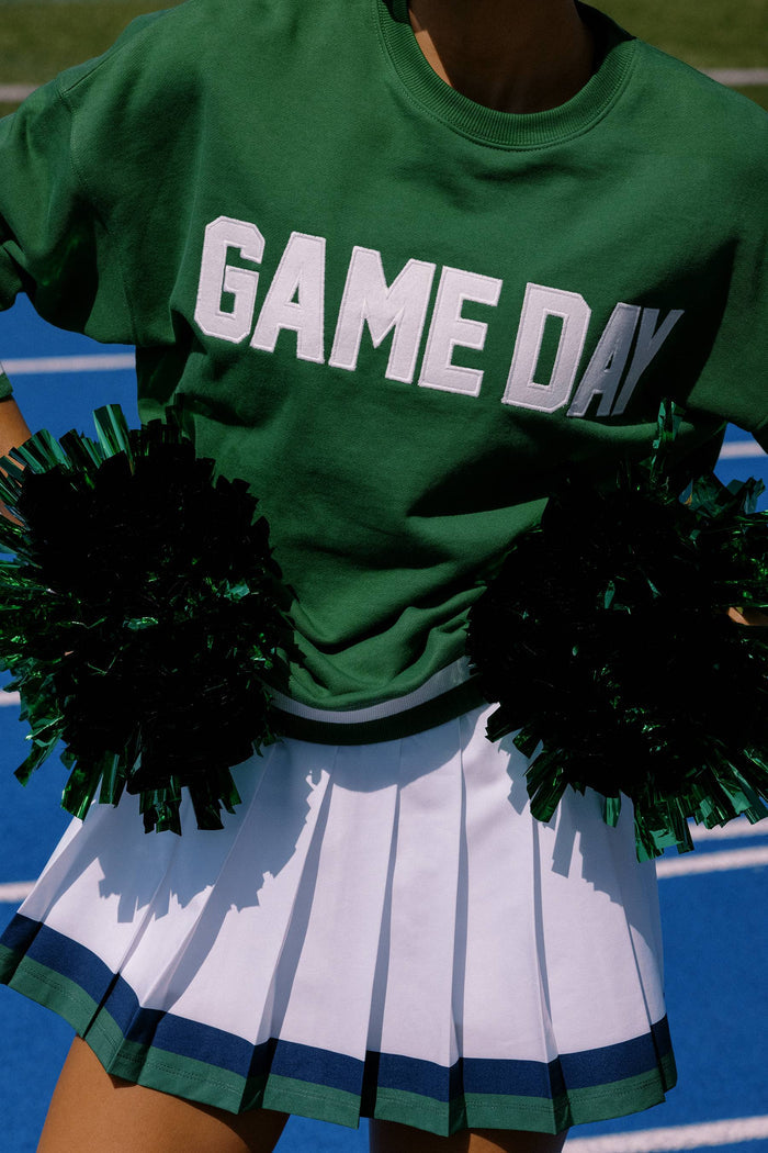 Person wearing a green 'GAME DAY' shirt with black pom-poms on a sports field.