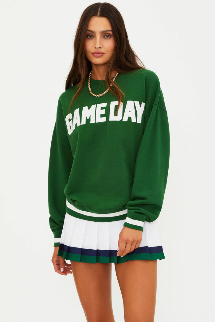 Woman wearing a green 'GAME DAY' sweatshirt and white skirt with green trim on a white background