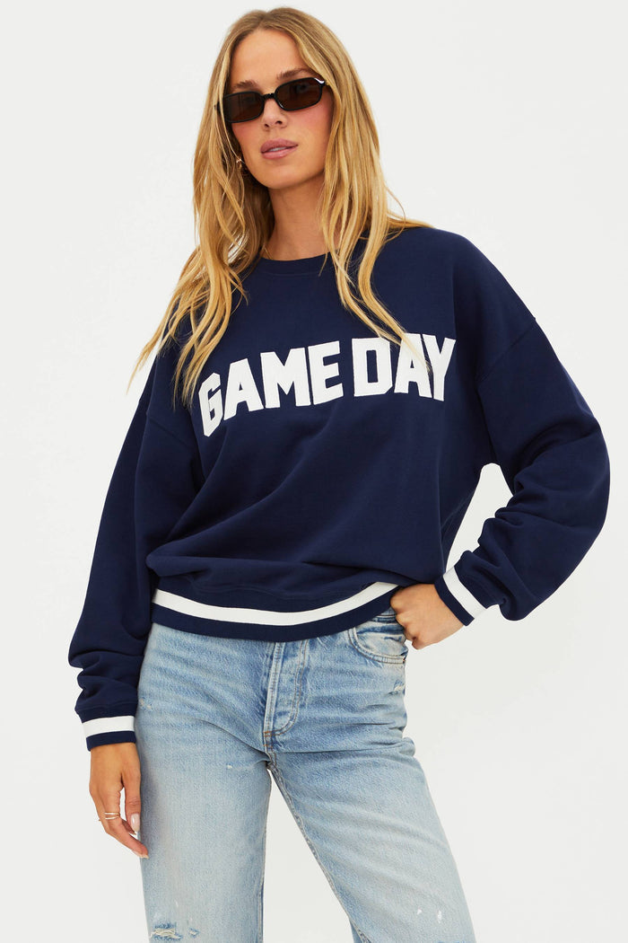 Woman wearing a navy 'GAMEDAY' sweatshirt and light blue jeans on a white background