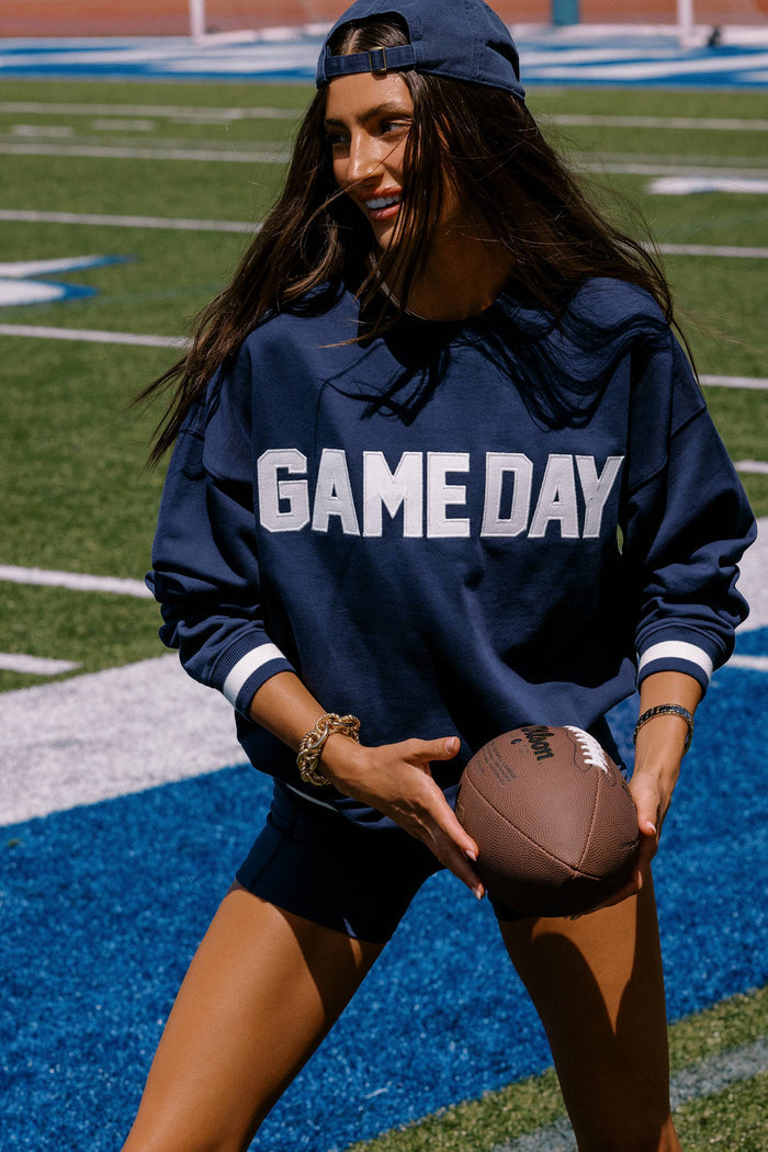 Person wearing a 'GAMEDAY' sweatshirt holding a football on a sports field.